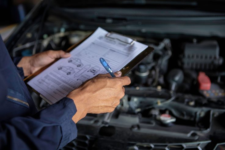 Repair technician holding a clipboard for repair quote inspecting vehicle damage