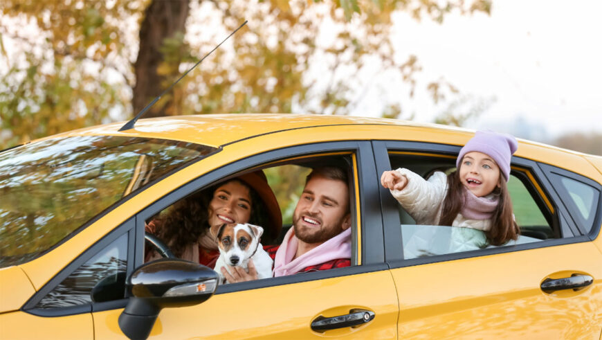 A woman, man, child, and a dog in a yellow car on a fall day.