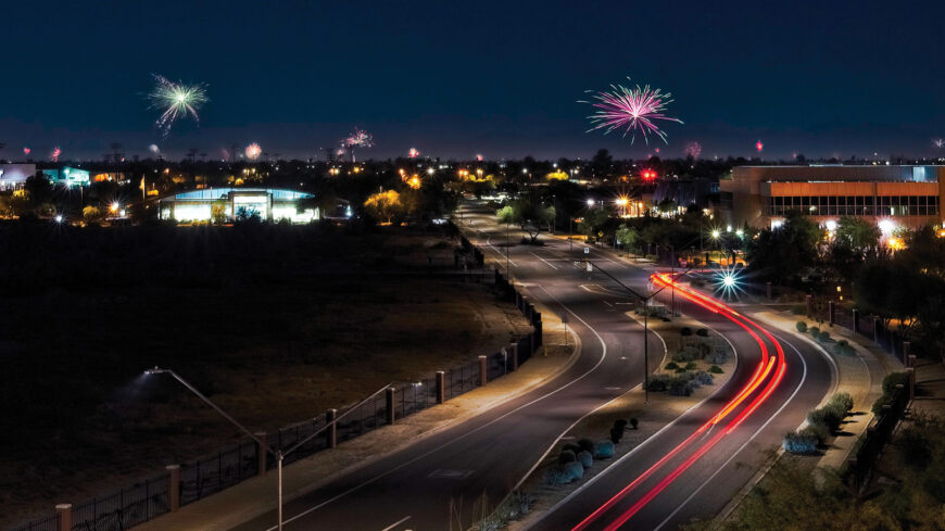 A city skyline with cars driving at night and fireworks exploding in the air